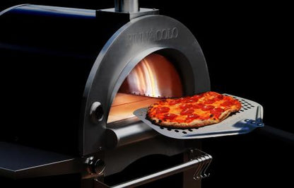 A pepperoni pizza with melted cheese is being removed with a pizza peel from the Fire One Up PINNACOLO IBRIDO Hybrid Wood/Gas Outdoor Pizza Oven, which has a visible flame inside.