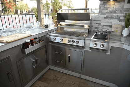 A modern outdoor kitchen with Kokomo Grills' Stainless Steel Two Drawer - One Door Combo (KO-ALPDC), gas grill, side burner, and utensils, all set against stone tile walls and a window.
