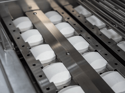 White tablets neatly lined up inside a metal machine, reminiscent of the precision found in the Kokomo Grills Mini Maui 6-Foot Kitchen Island by Kokomo Grills, with metallic dividers and rods visible above.