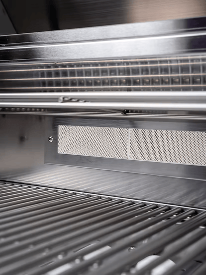 Close-up of clean, empty stainless steel grill grates inside a Kokomo Grills Mini Maui 6-Foot Kitchen Island, featuring a vented metal panel on the interior wall.