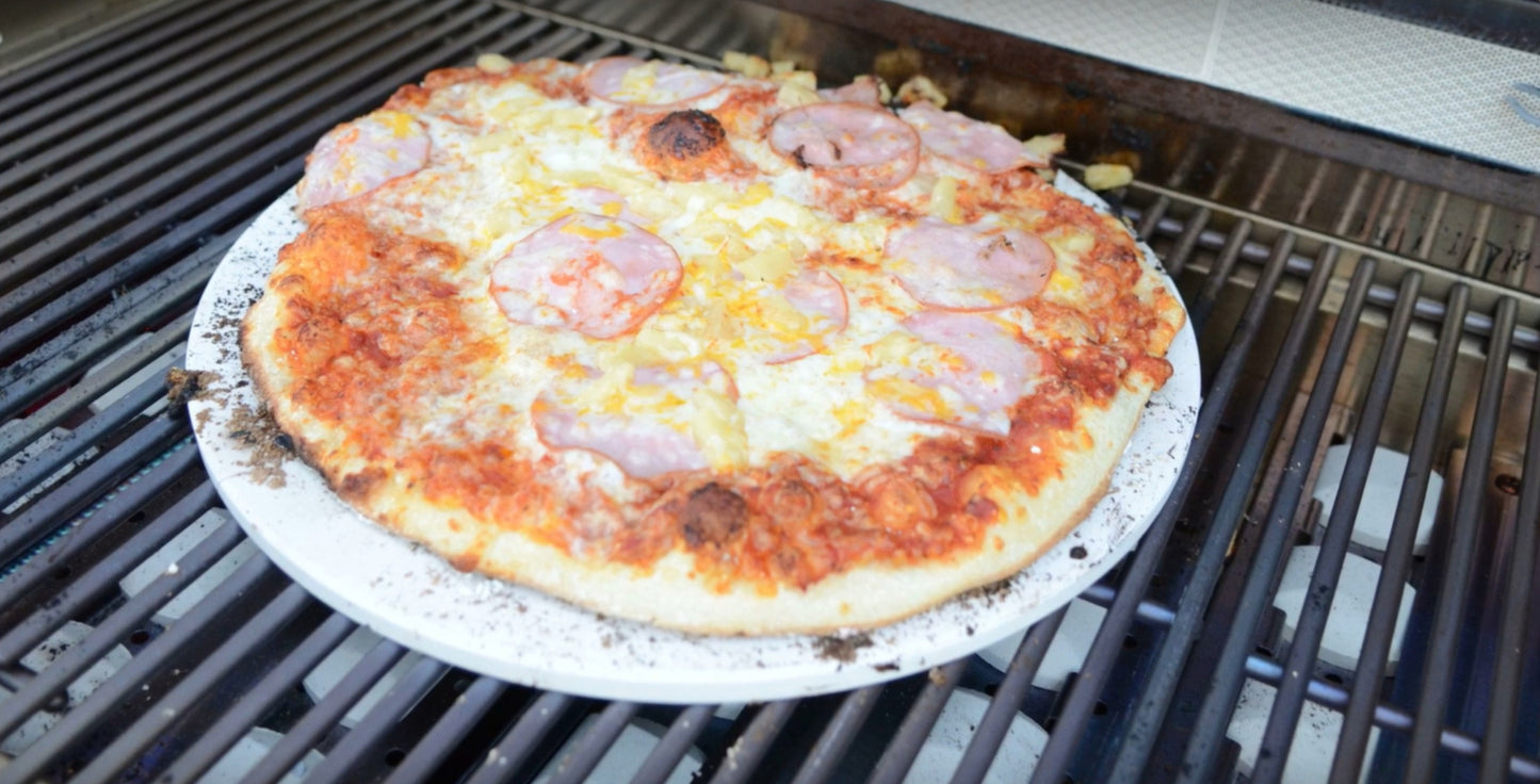 A delicious wood-fired ham and cheese pizza sits on a Kokomo Grills 14-Inch Pizza Stone Kamado Ceramic Oven Insert, its edges slightly burnt and cheese perfectly browned.