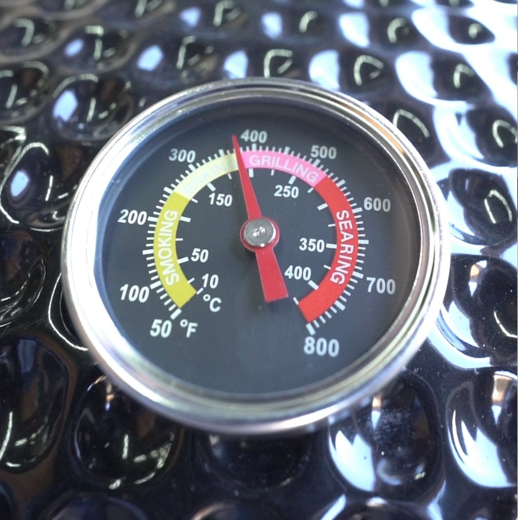 Close-up of a Kokomo Grills 21-Inch Kamado Ceramic BBQ Grill KO-21-KAMADO thermometer, displaying smoking, grilling, and searing zones in Fahrenheit and Celsius. Ideal for precision charcoal cooking by Kokomo Grills. Textured black background.