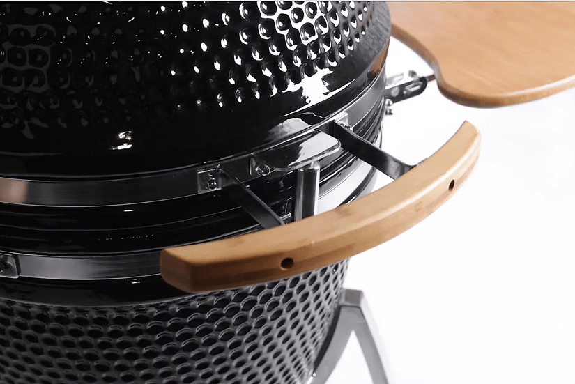 Close-up of the Kokomo Grills 21-Inch Kamado Ceramic BBQ Grill KO-21-KAMADO, featuring a black textured finish, wooden handle, and foldable wooden side shelf—ideal for charcoal grilling by Kokomo Grills, shown against a white background.