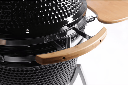 Close-up of the Kokomo Grills 21-Inch Kamado Ceramic BBQ Grill KO-21-KAMADO, featuring a black textured finish, wooden handle, and foldable wooden side shelf—ideal for charcoal grilling by Kokomo Grills, shown against a white background.