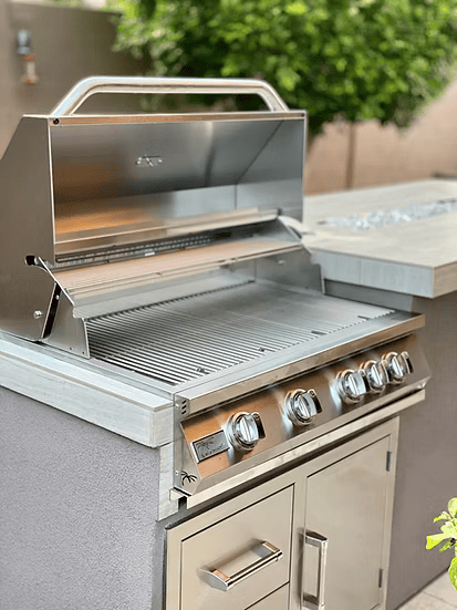 The Kokomo Grills 3-Piece Outdoor Kitchen Set—featuring a stainless grill, drawers, and cover—rests on a patio countertop, its open lid revealing a clean grate and making it a perfect fit for any stylish outdoor space.