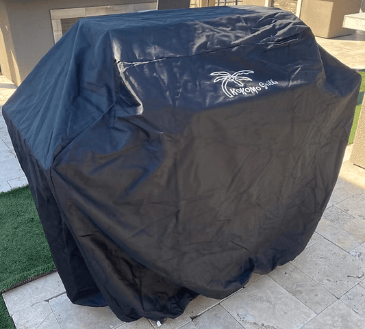 A Kokomo Grills 3 Burner Grill Cart is protected by a Kokomo Grills 26-inch grill cover, placed on a stone patio with green artificial turf nearby.
