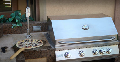 A fresh pizza on a wooden peel is ready to be baked beside the Kokomo Grills 40-Inch Professional Built-In Gas Grill (5 Burner) in an outdoor stone patio kitchen setup.
