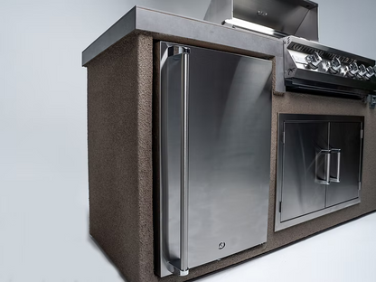 The Kokomo Grills 7-Foot Straight Kitchen Island features a stainless steel fridge, built-in Kokomo Grills with control knobs, and storage cabinets in a textured, stone-like enclosure.