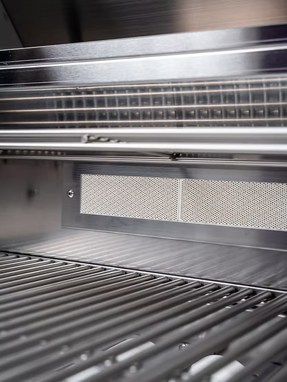 Close-up view of clean, empty metal grill grates inside a Kokomo Grills 7-Foot Straight Kitchen Island, with a ventilation or heat deflector panel visible at the back.