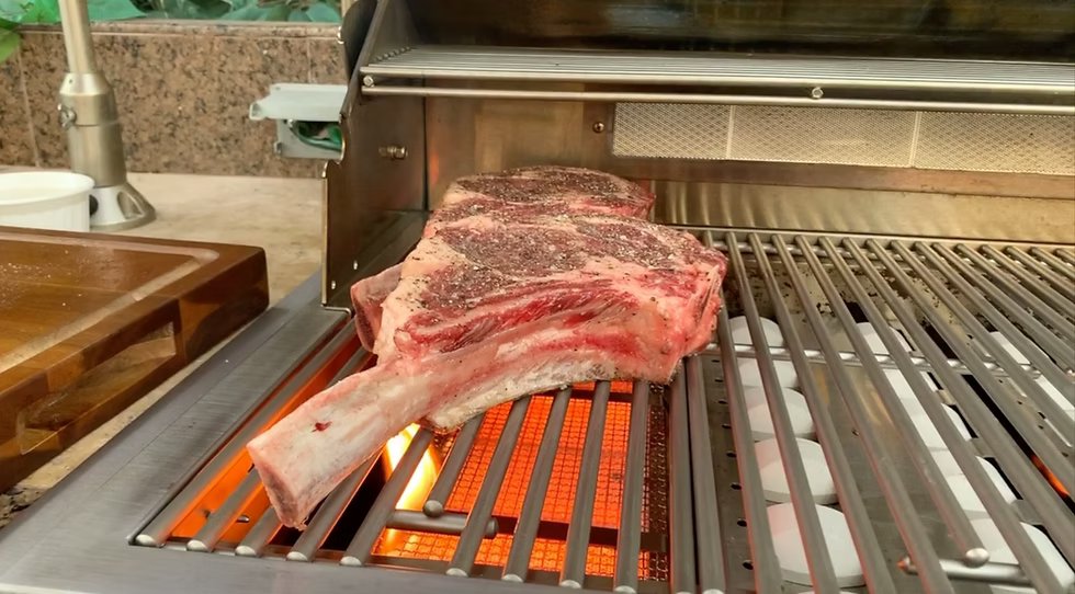 A large tomahawk steak sizzles over an open flame on a Kokomo Grills BBQ Grill, as the KO-IRSB Infrared Sear Zone Burner sears the meat and creates perfect grill marks.