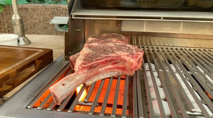 A large tomahawk steak sizzles over an open flame on a Kokomo Grills BBQ Grill, as the KO-IRSB Infrared Sear Zone Burner sears the meat and creates perfect grill marks.