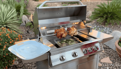 A Kokomo Grills BBQ Grill Rotisserie Kit by Kokomo Grills slowly roasts two chickens and a tray of vegetables on a stainless steel outdoor grill, set in a backyard with lush plants, stones, and a brick wall in the background.