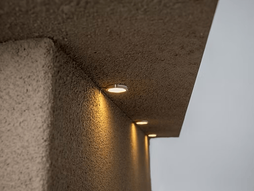Close-up of a textured concrete ceiling with three warm recessed lights shining down a matching wall, creating the perfect ambiance to enjoy your Kokomo Grills Baja with Fire 7.5’ x 9’ Kitchen Island by Kokomo Grills in a cozy outdoor setting.