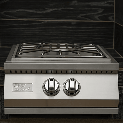 The Kokomo Grills Built-In Power Burner with Removable Grate for Wok is a stainless steel gas stove featuring two burners, each operated by a large round front knob, and set against a dark wood-patterned backsplash.