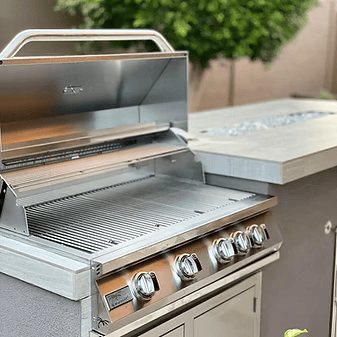 A close-up of the Kokomo Grills 5 Burner 40-Inch Cart Model BBQ Grill with its lid open, displaying clean grill grates and control knobs on a stainless steel cart with locking casters, set on a backyard patio.