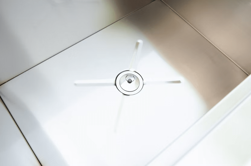 Close-up of a clean, modern stainless steel sink with a circular drain and four diagonal lines, echoing the sleek design of the Kokomo Grills Drop-In Stainless Steel Ice Chest 23 x 17 KO-AIC by Kokomo Grills.