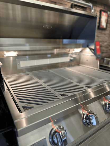 A close-up of a Kokomo Grills gas grill with the lid open, showcasing Kokomo Grills LuxCut Laser-Cut Culinary Grates and three front control knobs, set in a modern kitchen or patio.