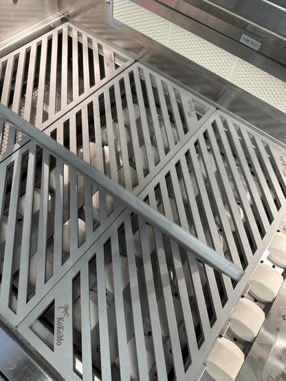 Close-up of Kokomo Grills LuxCut Laser-Cut Culinary Grates for 3, 4, 5 Burner Classic and Pro Grills, showing diagonal slots, a metal bar on the 304 stainless steel surface, and distinctive Kokomo branding etched on the grates.