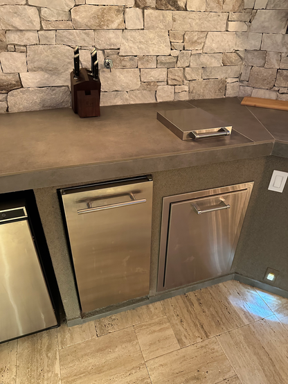 A modern kitchen countertop with knife block, metal tray, and stone backsplash sits above stainless steel dishwasher and cabinets—ideal for pairing with the Kokomo Grills Luxury Outdoor Kitchen BBQ Grill Island by Kokomo Grills.