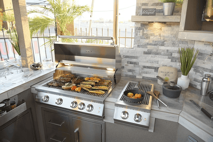 Sunny patio outdoor kitchen featuring a stainless steel grill for meat and veggies, potted plants, modern stone backsplash, and a Kokomo Grills Professional Double Side Burner with Removable Cover for your pot and pan cooking.