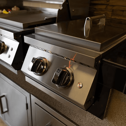 A close-up of the Kokomo Grills KoKoMo Grills Professional Double Side Burner with Removable Cover, featuring two large control knobs and a closed lid, set against a modern kitchen background.
