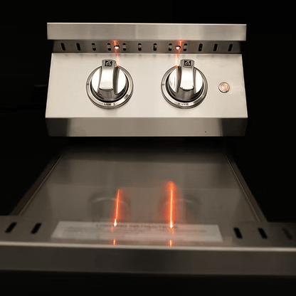Close-up of the KoKoMo Grills Professional Double Side Burner with removable cover by Kokomo Grills. The stainless steel unit has two control knobs set to low, glowing orange indicator lights, and a clean, reflective surface against a dark background.