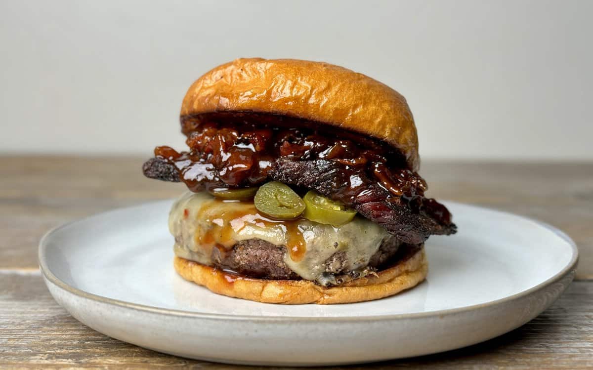 A cheeseburger on a glossy brioche bun with melted cheese, pickles, crispy bacon, and caramelized onions—fresh off the Kokomo Grills Professional Griddle 30-Inch Outdoor Kitchen Teppanyaki Flat Grill by Kokomo Grills.