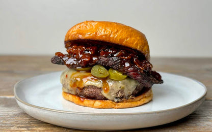 A cheeseburger on a glossy brioche bun with melted cheese, pickles, crispy bacon, and caramelized onions—fresh off the Kokomo Grills Professional Griddle 30-Inch Outdoor Kitchen Teppanyaki Flat Grill by Kokomo Grills.