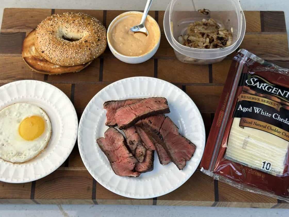 A sesame bagel, sliced steak, and sunny-side-up egg, topped with caramelized onions, sauce, and white cheddar—perfectly prepared on the Kokomo Grills Professional Griddle 30-Inch Outdoor Kitchen Teppanyaki Flat Grill.
