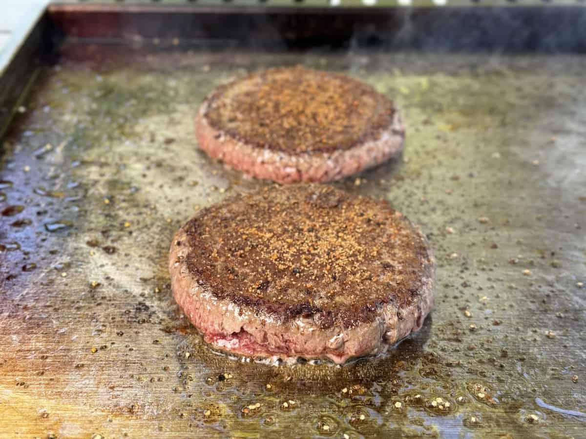 Two beef patties sizzle on the Kokomo Grills Professional Griddle 30-Inch Outdoor Kitchen Teppanyaki Flat Grill, their surfaces browning perfectly on its 304 stainless steel.