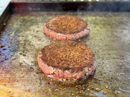Two beef patties sizzle on the Kokomo Grills Professional Griddle 30-Inch Outdoor Kitchen Teppanyaki Flat Grill, their surfaces browning perfectly on its 304 stainless steel.