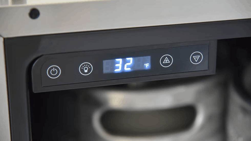 Close-up of the digital control panel on the Kokomo Grills Professional Luxury Outdoor Kitchen Kegerator KO-LUX-KEG, showing 32°F. The sleek stainless steel unit features power, light, and adjustment buttons, with a metal keg visible inside.