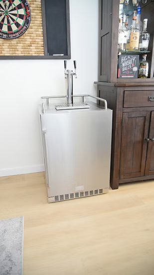 A Kokomo Grills Professional Luxury Outdoor Kitchen Kegerator KO-LUX-KEG with a dual tap draft system stands beside a dark wooden liquor cabinet, while a dartboard is mounted on the wall above.