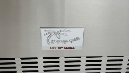 A metal plate on the Kokomo Grills Professional Luxury Outdoor Kitchen Kegerator KO-LUX-KEG features a palm tree graphic and “Kokomo Grills” above a vented grill, ideal for your kegerator or outdoor kitchen setup.