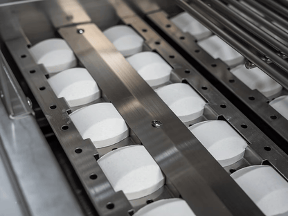 Rows of white circular tablets move along an automated production line, guided by metal components with precision—much like assembling a Kokomo Grills St. John 7-Foot and 6-Inch Kitchen Island from Kokomo Grills.