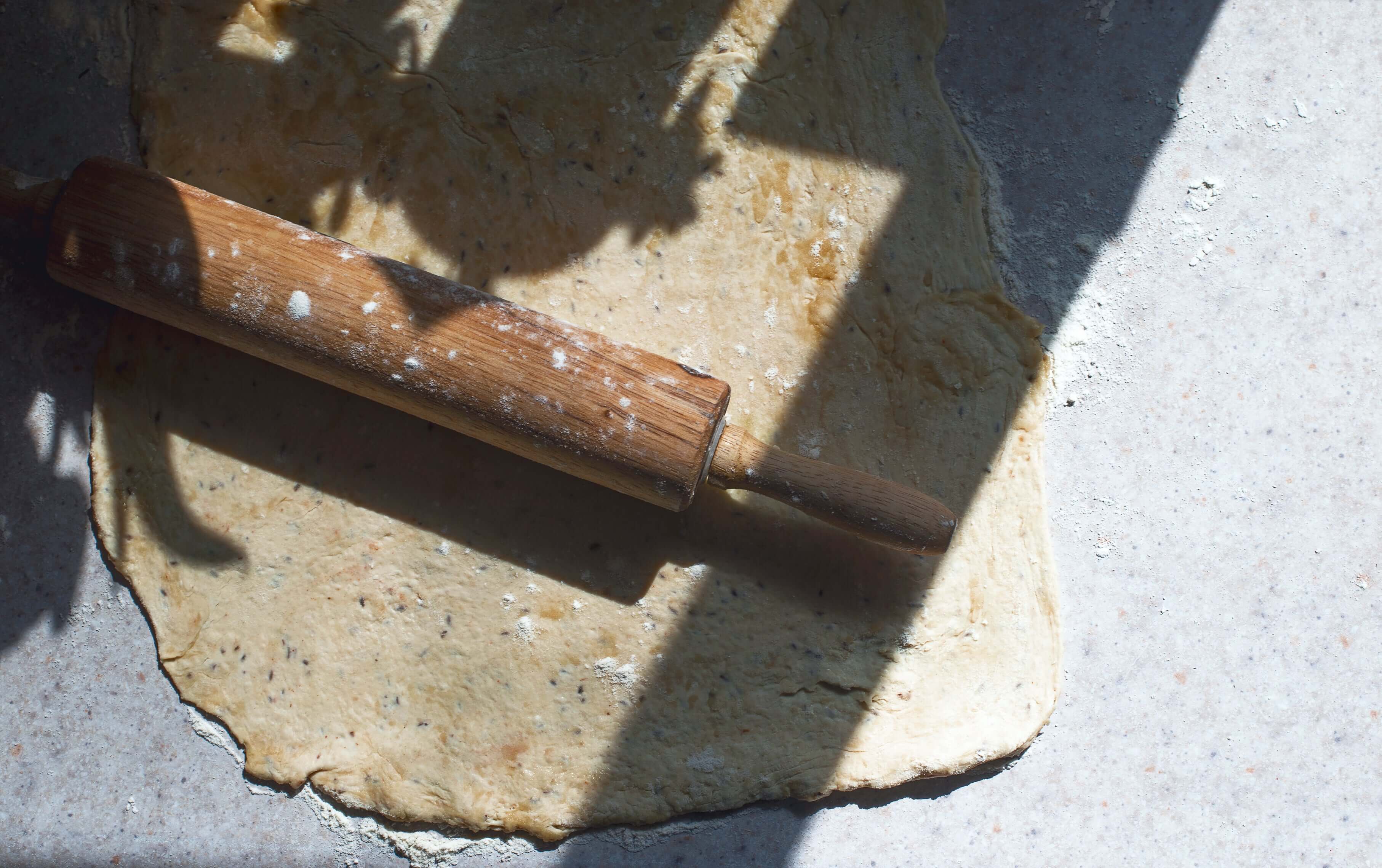 A wooden rolling pin rests on top of rolled-out dough on a gray marble countertop.