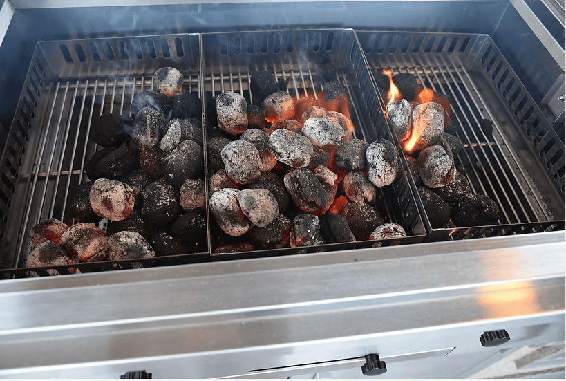A close-up of the Kokomo Grills 32-Inch Built-In Charcoal Grill, made from 304 stainless steel, shows black and gray briquettes burning with flames and glowing embers—ideal for any outdoor kitchen.