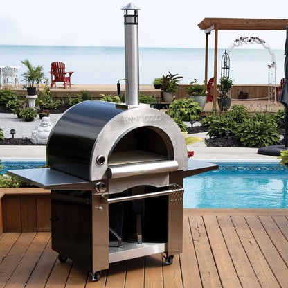 The Fire One Up PINNACOLO IBRIDO Hybrid Wood/Gas Outdoor Pizza Oven sits on a wooden deck by the pool, offering lake views under sunny skies and delivering perfect pizzas every time.