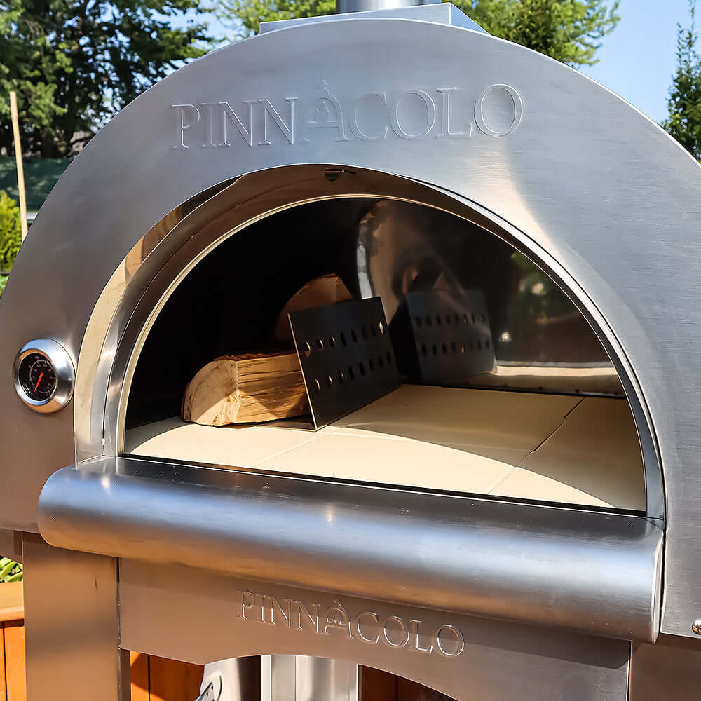 Zoomed-out view of the PINNACOLO PREMIO Wood Fired Outdoor Pizza Oven with an empty surface, except for a wooden log and metal separator placed on the left.