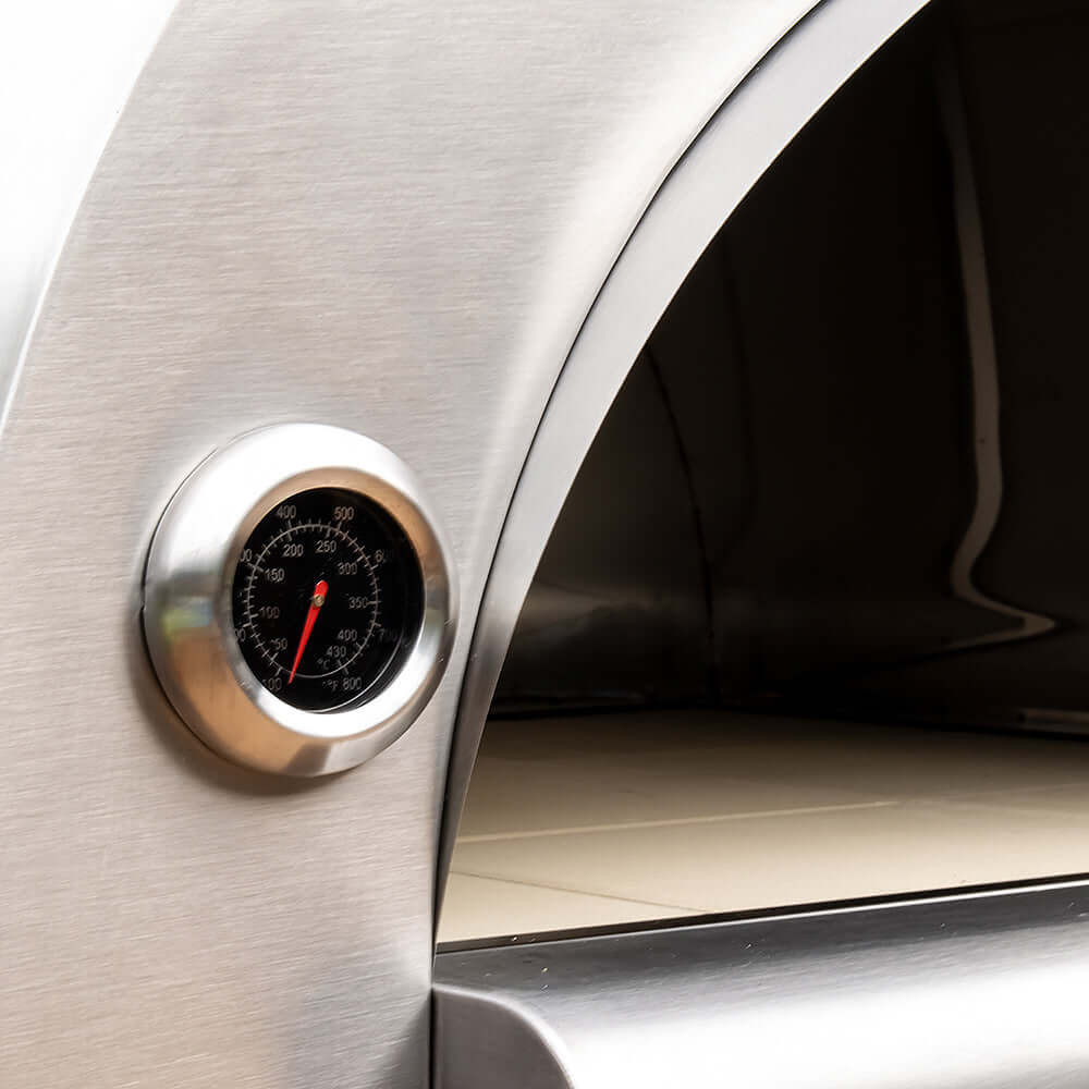 Close-up view of the PINNACOLO PREMIO Wood-Fired Outdoor Pizza Oven's empty cooking surface, showing the white firebrick and temperature gauge on the outer side wall.