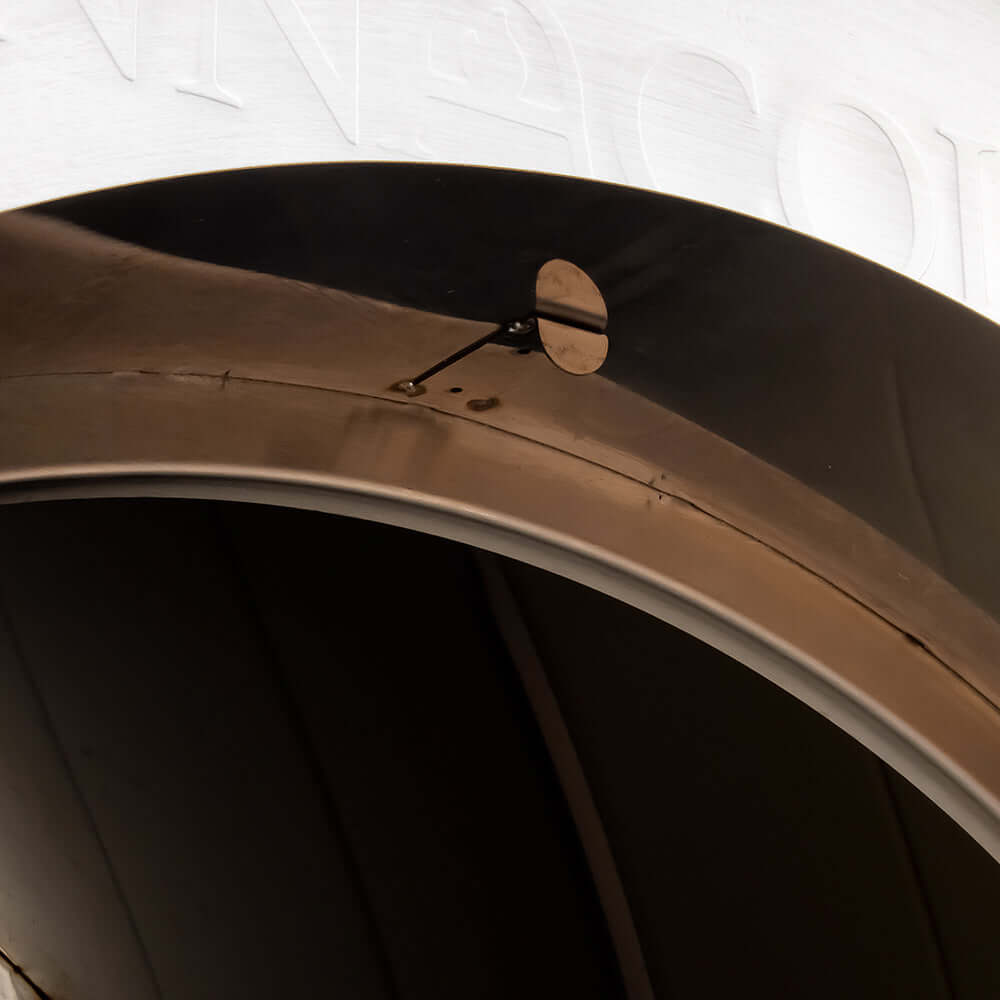 Close-up of a metallic surface with a circular arc, similar to the sleek design of the Fire One Up PINNACOLO PREMIO Wood Fired Outdoor Pizza Oven, featuring a small round protrusion near the center and faint embossed text on the upper section against a lighter background.
