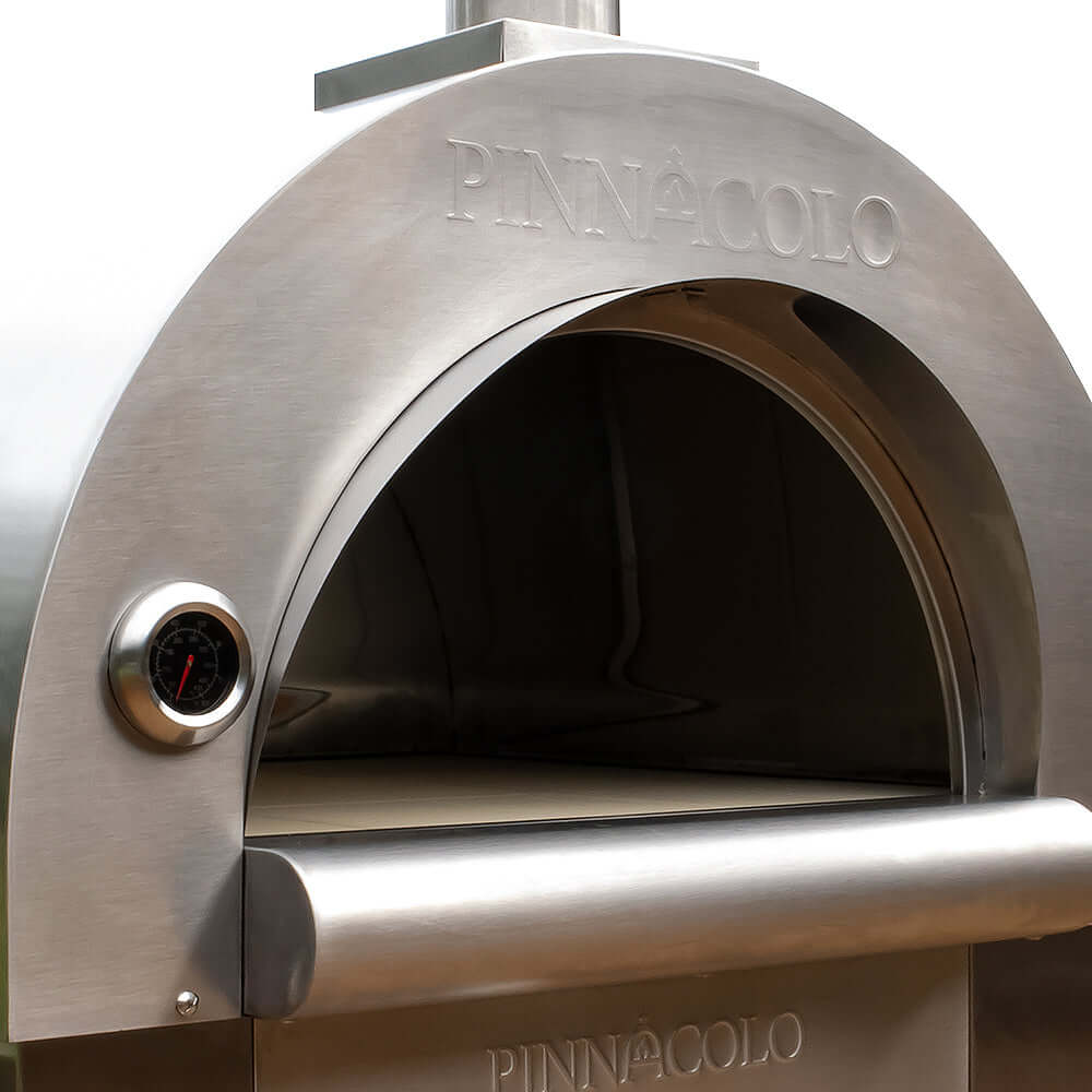 Full zoomed-out view of the PINNACOLO PREMIO Wood-Fired Outdoor Pizza Oven's empty cooking surface, showing the white firebrick and temperature gauge on the outer side wall, with the 'PINNACOLO' logo visible.