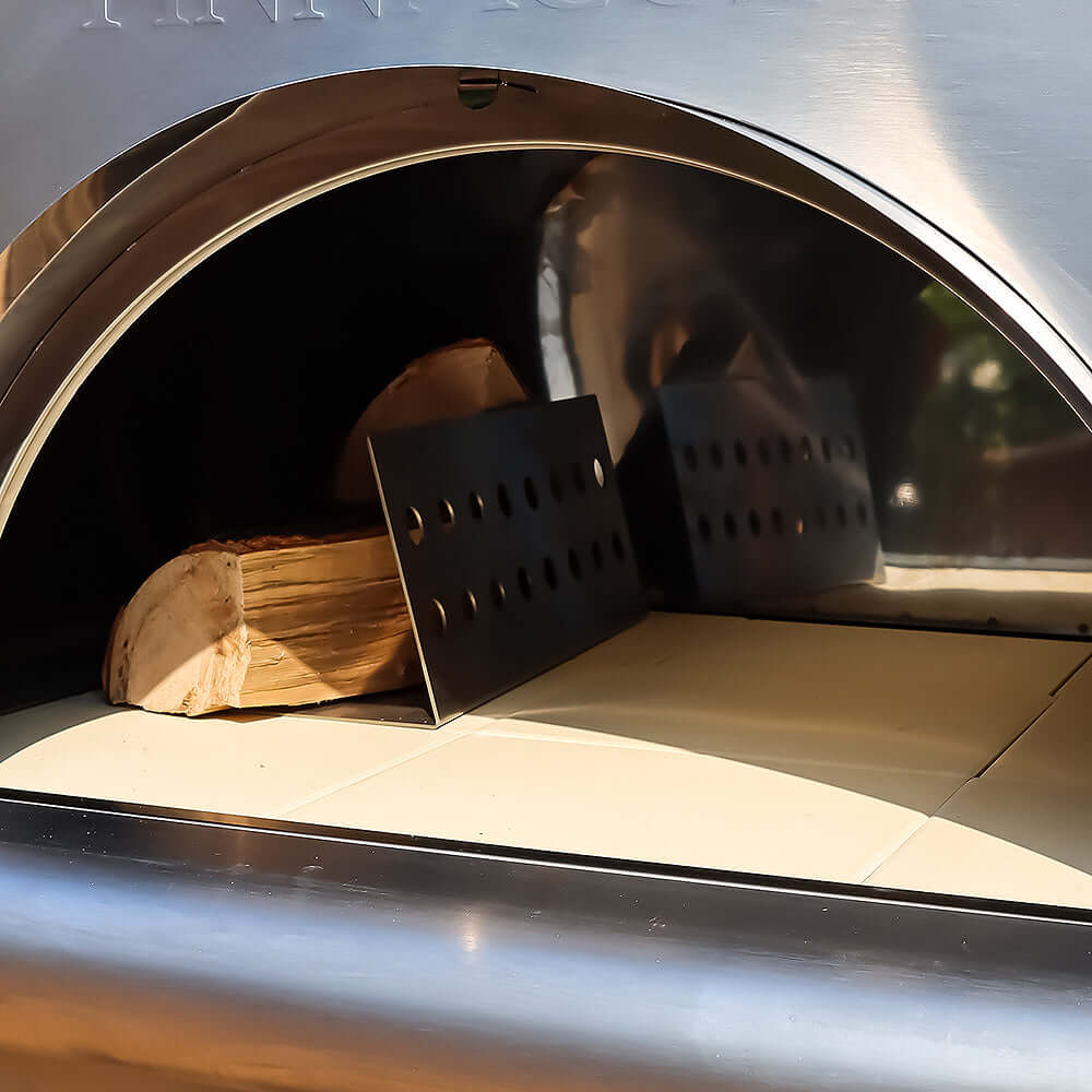 PINNACOLO PREMIO Wood-Fired Outdoor Pizza Oven with an empty surface, except for a wooden log and metal separator placed on the left.