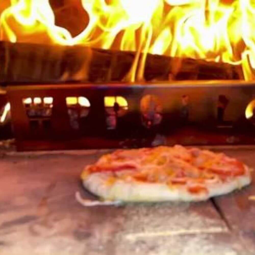 Pizza pie baking inside the Kokomo 32” Outdoor Wood-Fired Stainless Steel Pizza Oven, with flames visible in the background.