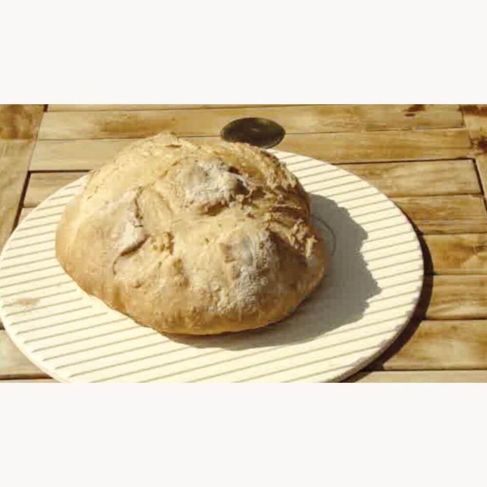 Wood-fired oven-baked loaf of bread on a round striped plate, placed on a wooden table.