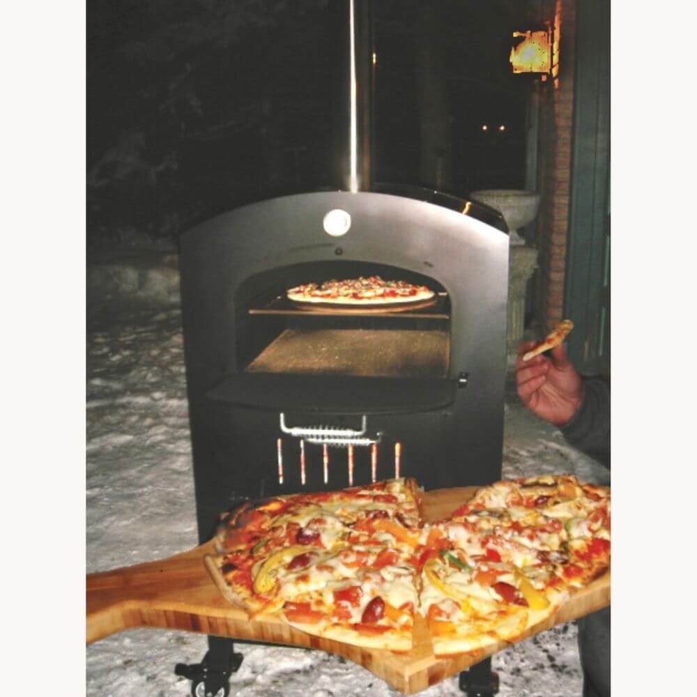 Tuscan Chef Medium Portable Family Pizza Oven with Cart (Model GX-C2) – A couple of people eating a slice of pizza, with two vegetable-topped pizzas on a wooden board beside them. Snow is visible on the ground.