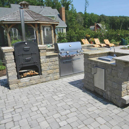 Tuscan Chef Medium Built-In Deluxe Family Pizza Oven (Model GX-CM) without cart, built into a stylish outdoor kitchen with a gas grill and sink on a paved patio, with a gazebo and lounge chairs in the background.