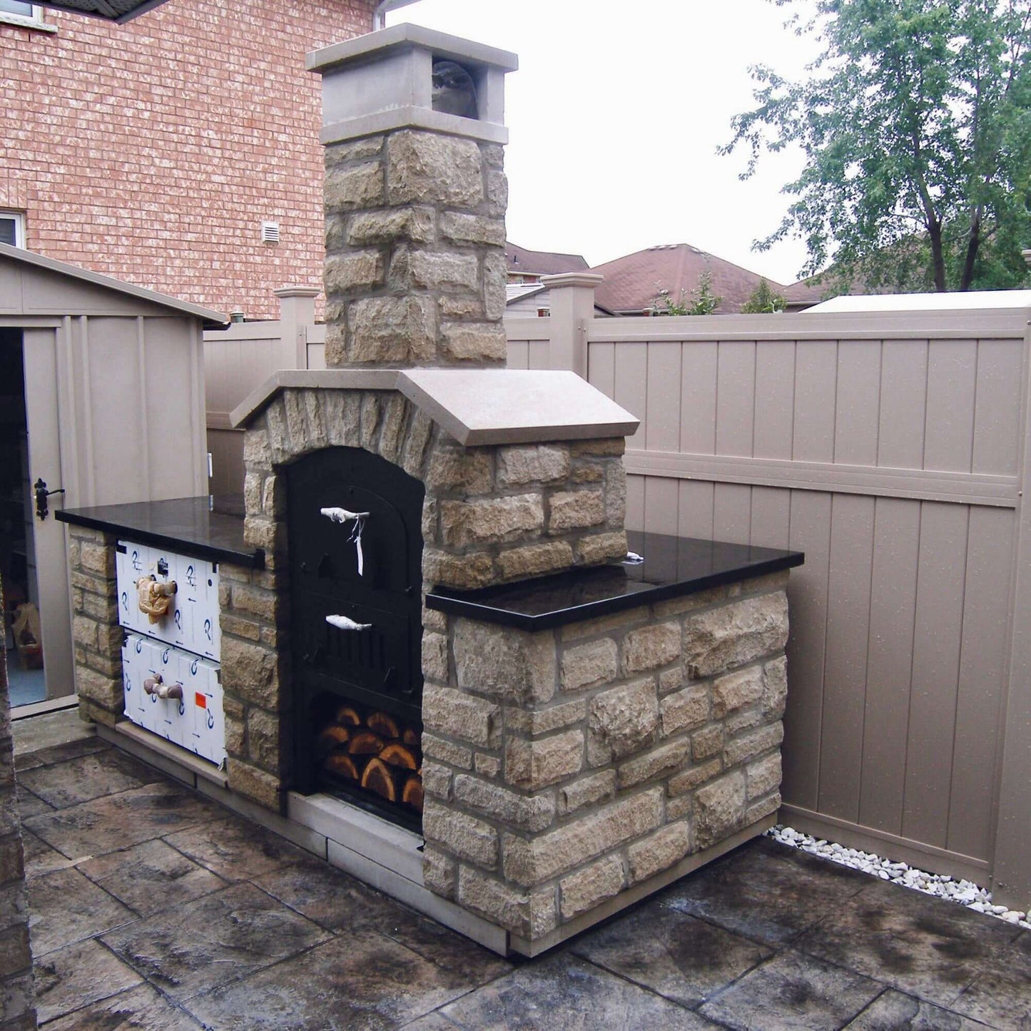 Tuscan Chef Medium Built-In Deluxe Family Pizza Oven (Model GX-CM) – Installed in a stone enclosure with a black countertop in the backyard.