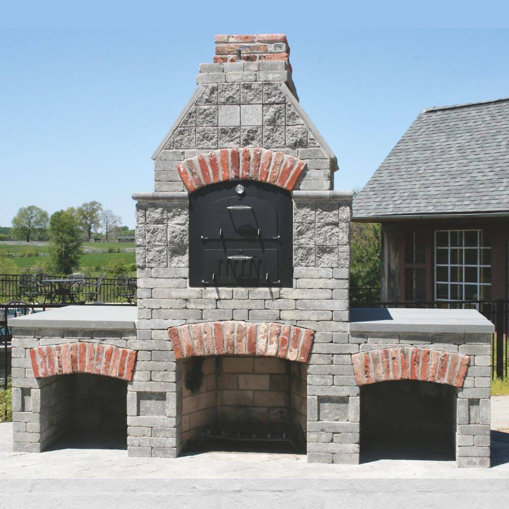 Tuscan Chef Medium Built-In Deluxe Family Pizza Oven (Model GX-CM) without cart, housed in a multi-chamber gray stone arched enclosure. The oven is situated on a patio with a house in the background.