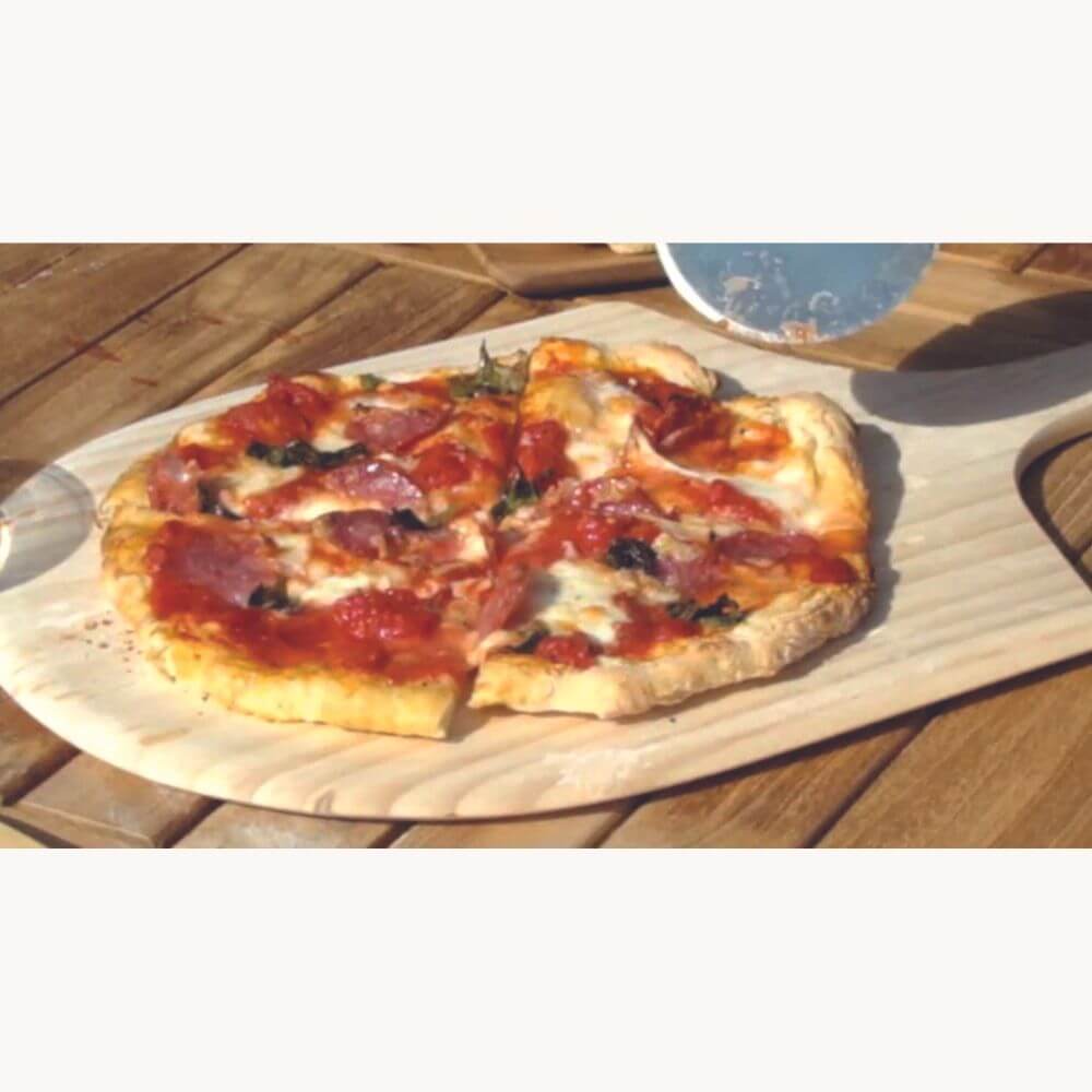 Three-meat pizza on a wooden peel, freshly pulled from a wood-fired oven to the table.